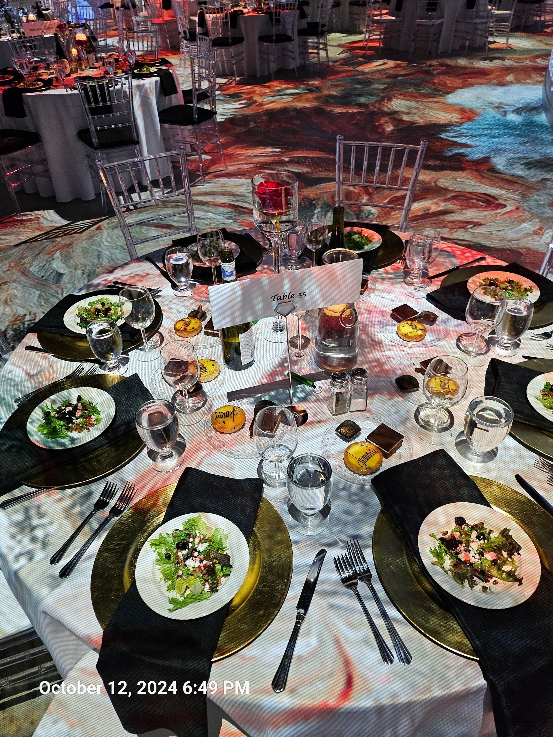 A formal round dinner table set for an event with place settings, salads, and drinks on a patterned carpeted floor.