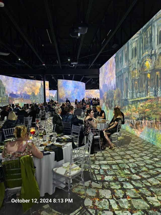 People dining at tables in a room with walls and floors projected with classic impressionist paintings.