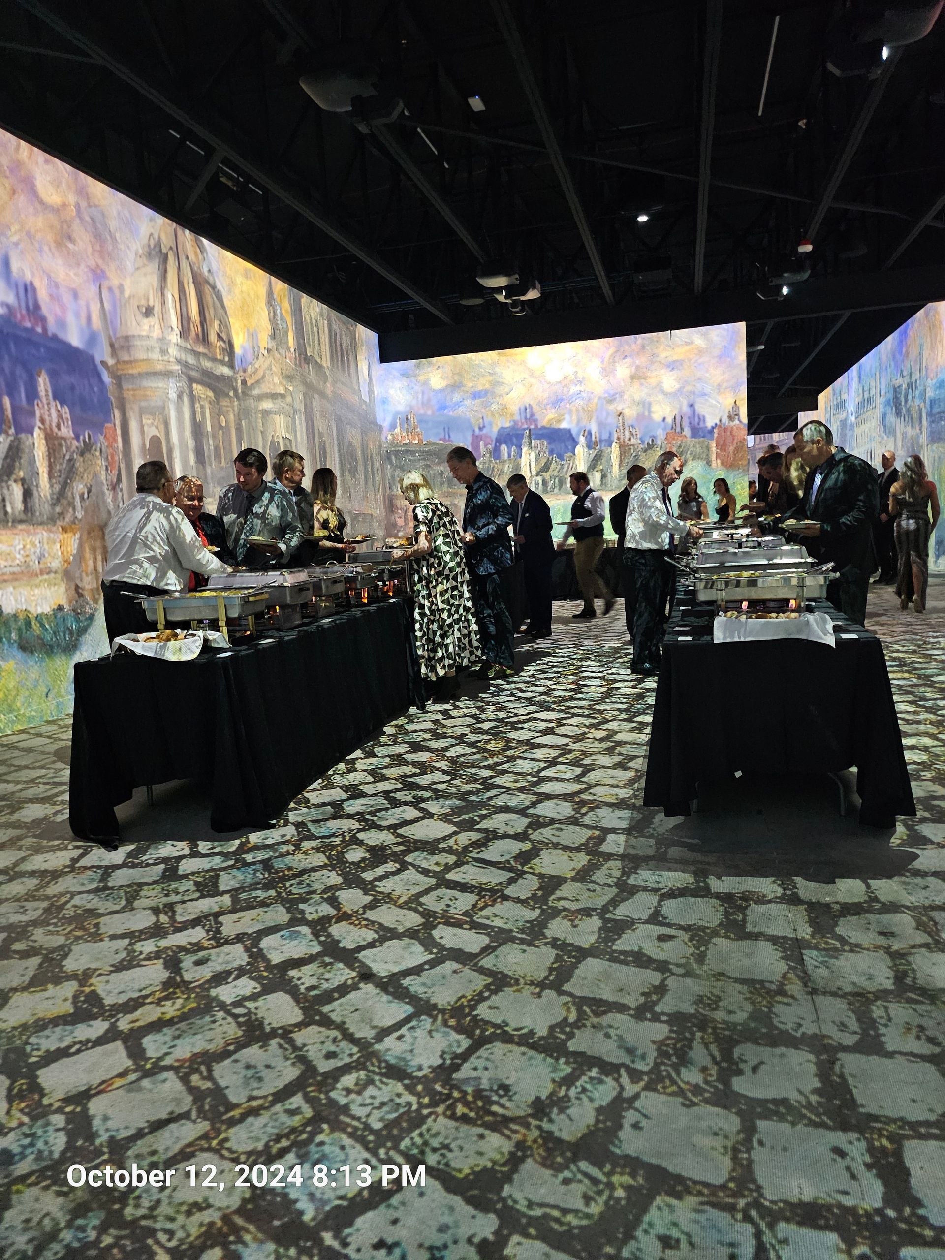 A catered event held in an immersive gallery with projections of impressionist paintings on the walls and stone floor.