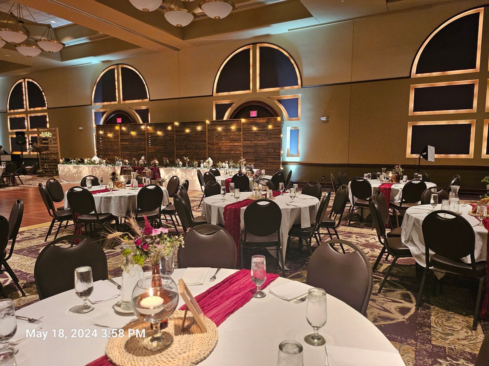 A banquet hall set for a formal event with round tables featuring white tablecloths, pink runners, and centerpieces.