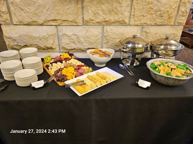 A buffet table set with stacks of white plates, a charcuterie board, bread, serving dishes, and a salad bowl.