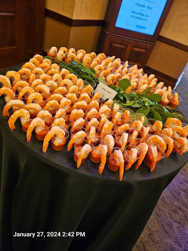 A round table covered in a black cloth features numerous individual shrimp cocktail servings garnished with fresh greens.