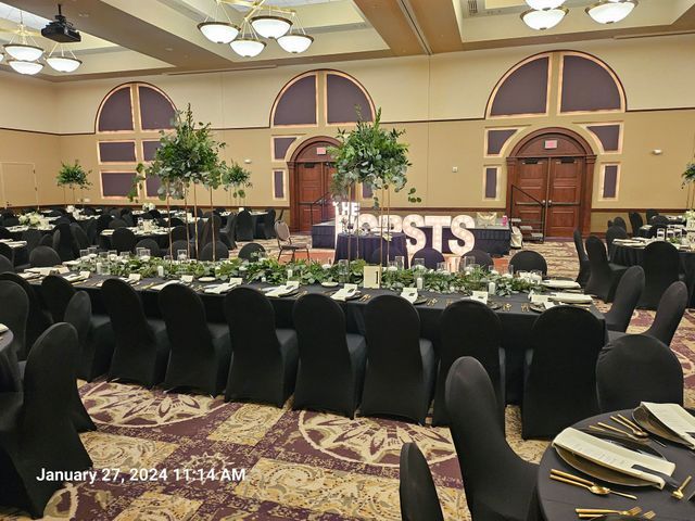 A banquet hall set for a wedding, featuring long tables with black tablecloths, floral centerpieces, and a 