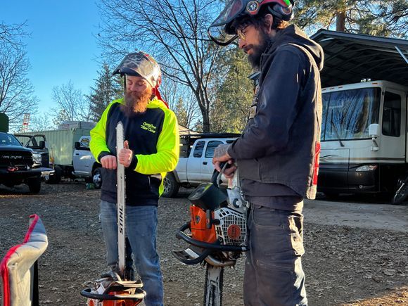 Two men are standing next to a chainsaw in a parking lot.