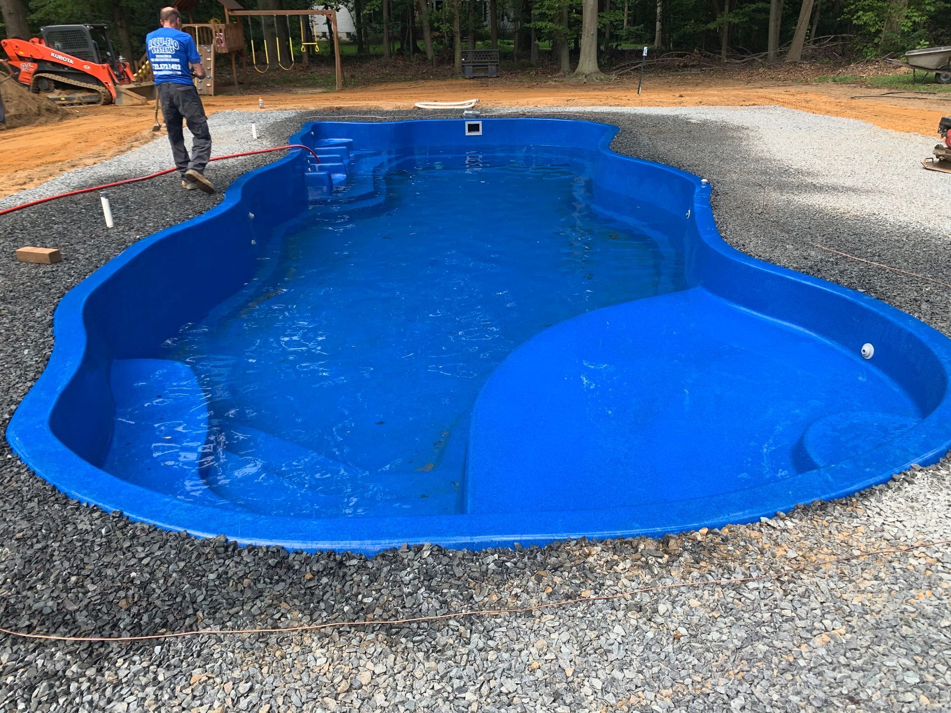 A man is standing next to a large blue swimming pool.