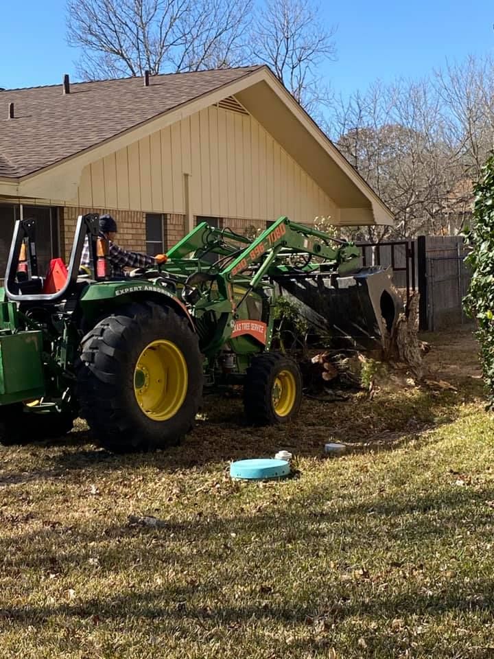 Green John Deere tractor with bucket clearing yard debris next to a house.