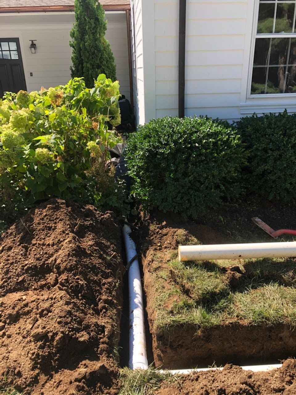A pipe is being installed in the dirt in front of a house.