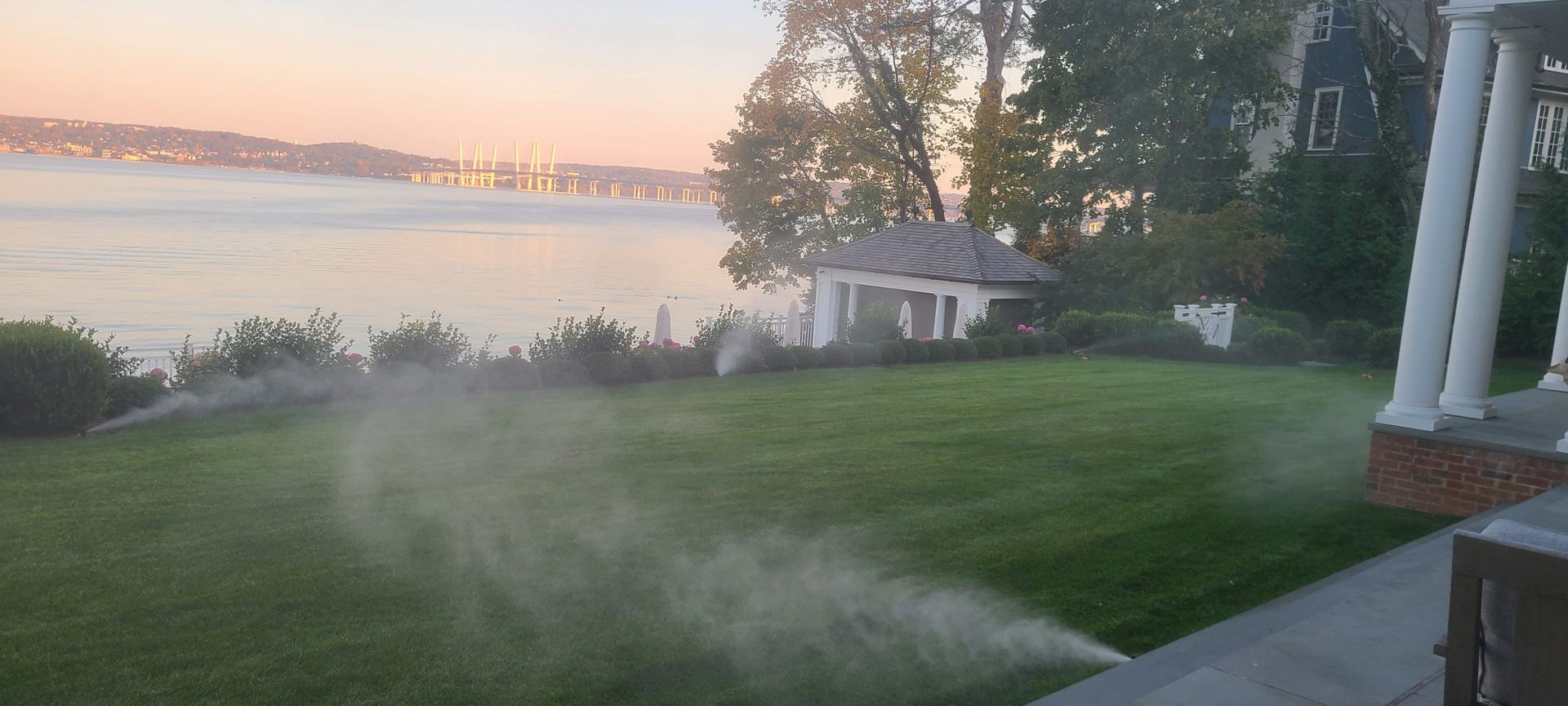 A sprinkler is spraying water on a lush green lawn next to a body of water.