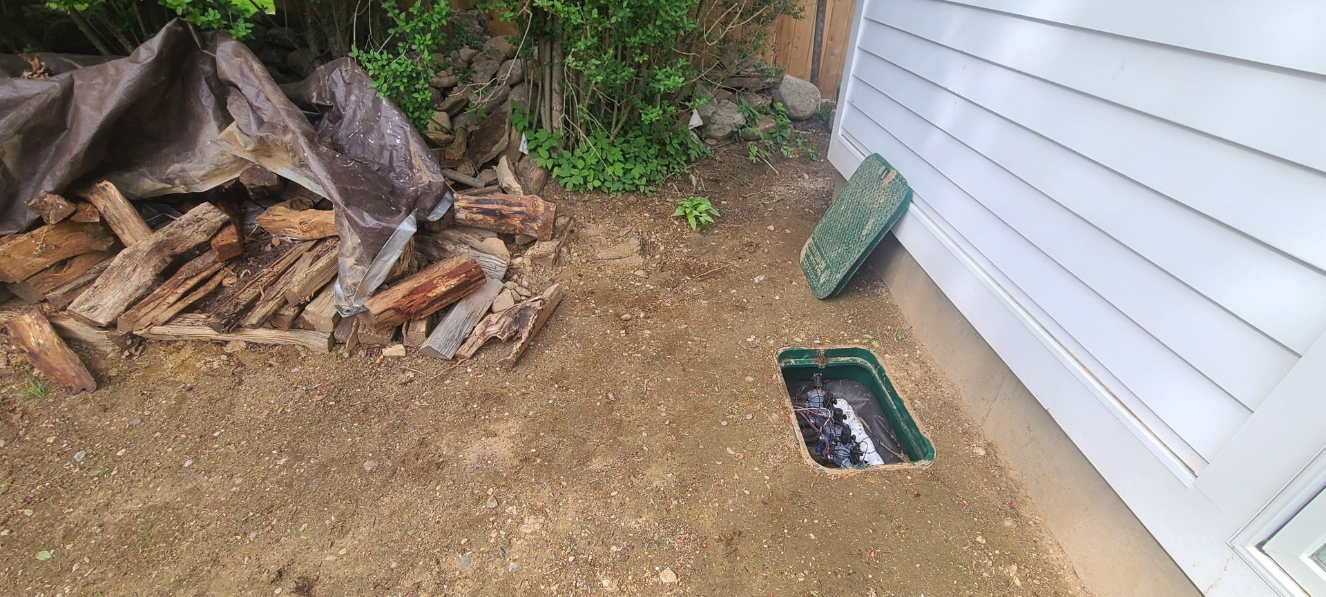 A pile of wood is sitting in the dirt next to a house.