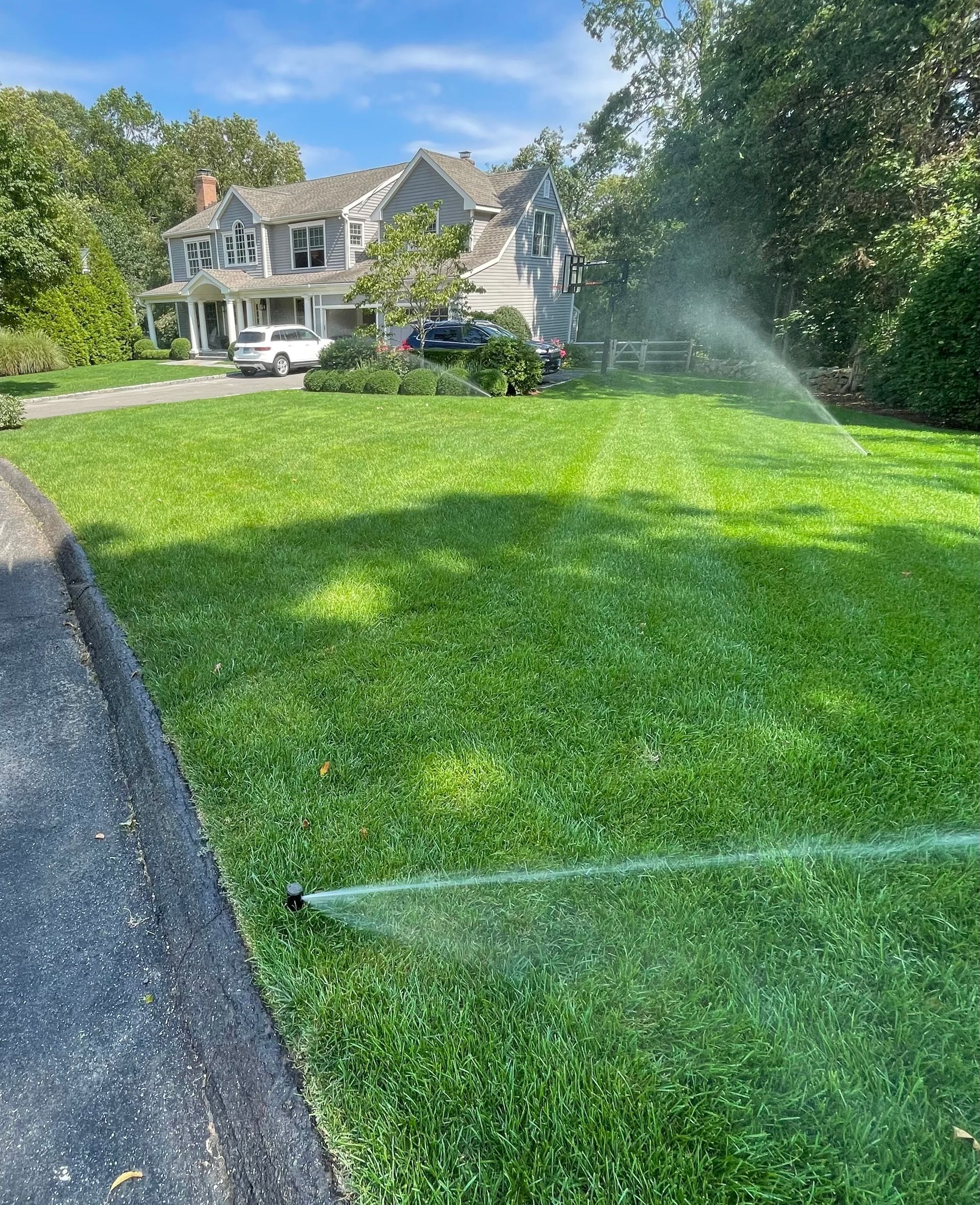 A sprinkler is spraying water on a lush green lawn in front of a house.
