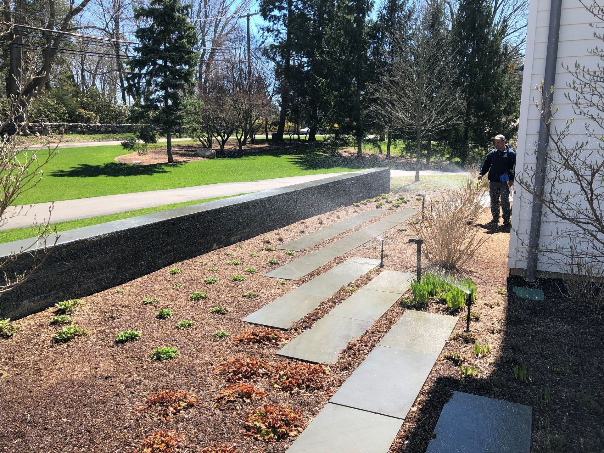 A man is standing next to a sprinkler in a garden.