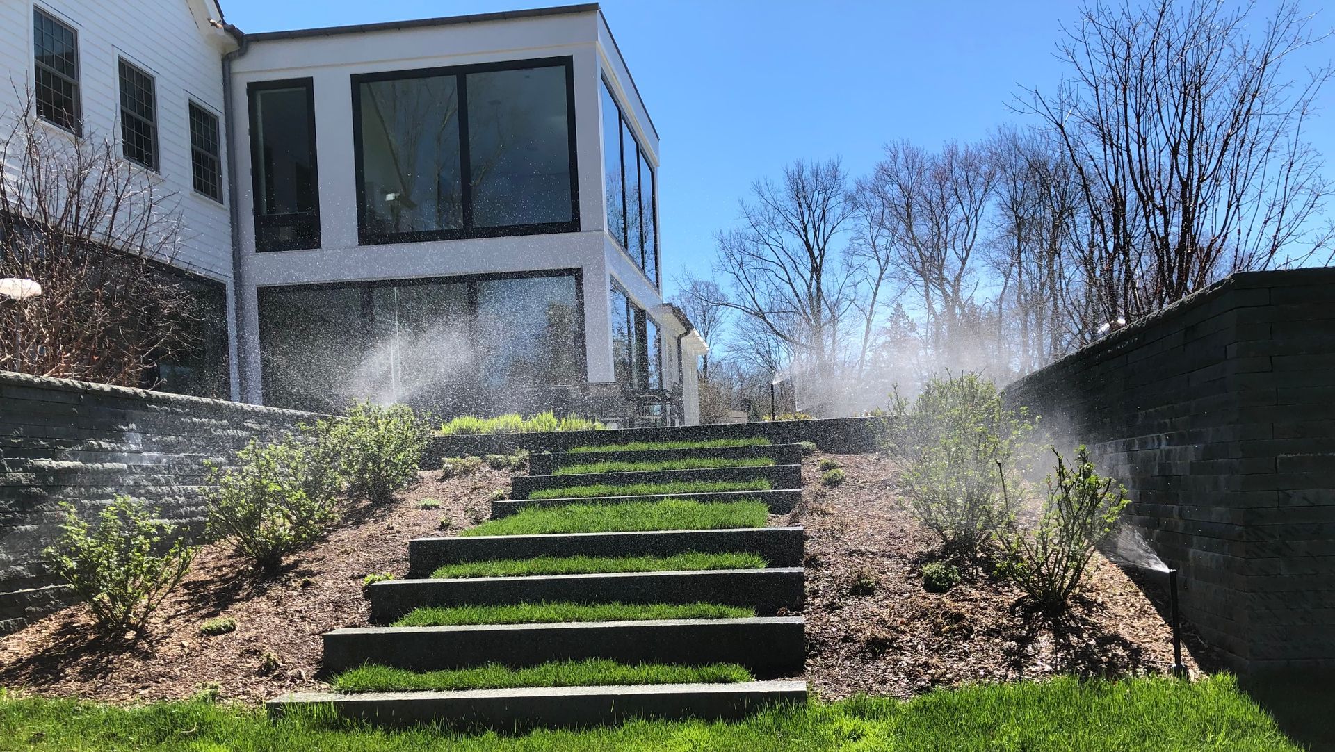 A house with stairs leading up to it and sprinklers spraying water on the grass.