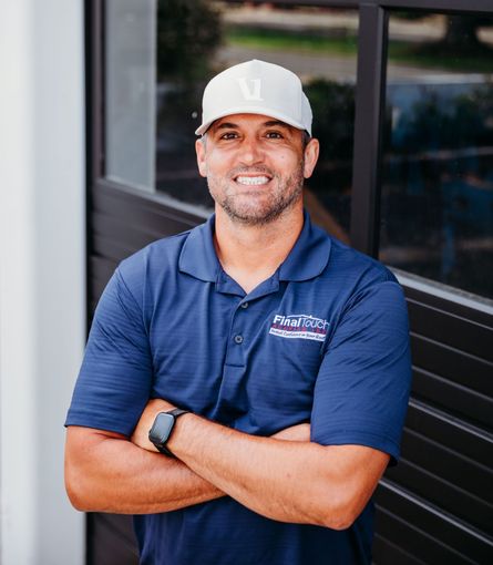 A man wearing a hat and a blue shirt is standing with his arms crossed.