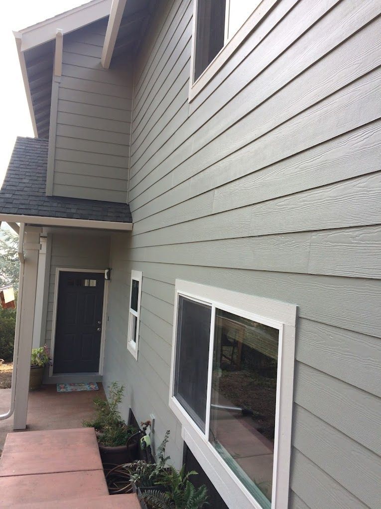 A house with a gray siding and white windows has a black door.