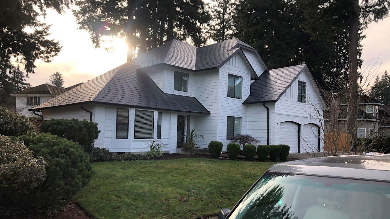 A white house with a black roof and a car parked in front of it.