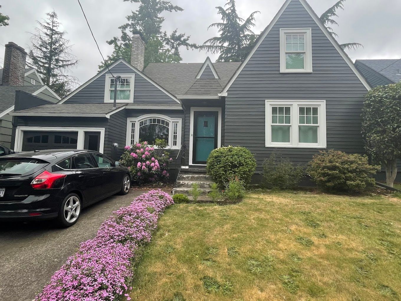 A black car is parked in front of a large house.