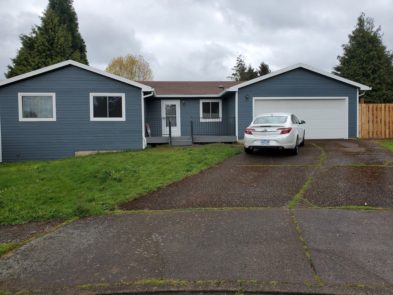 A white car is parked in front of a blue house.