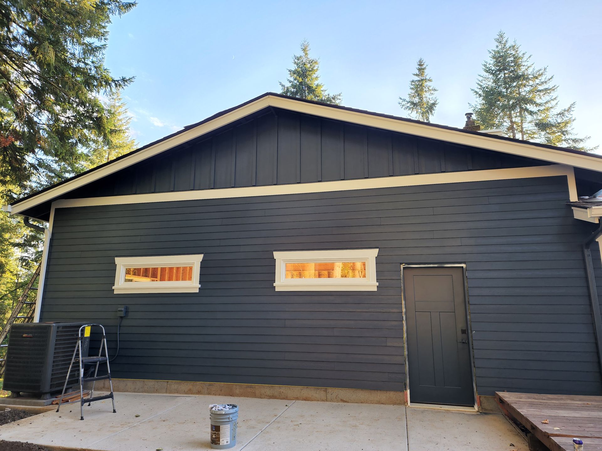 A black house with white trim is being painted.