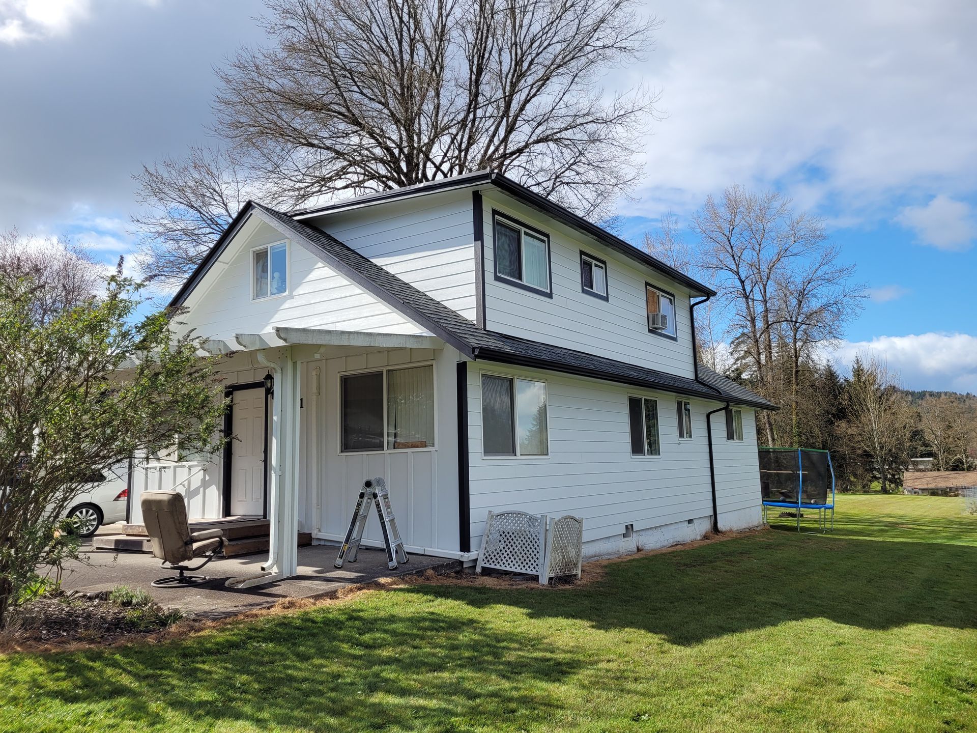 A white house with a black roof is sitting on top of a lush green field.