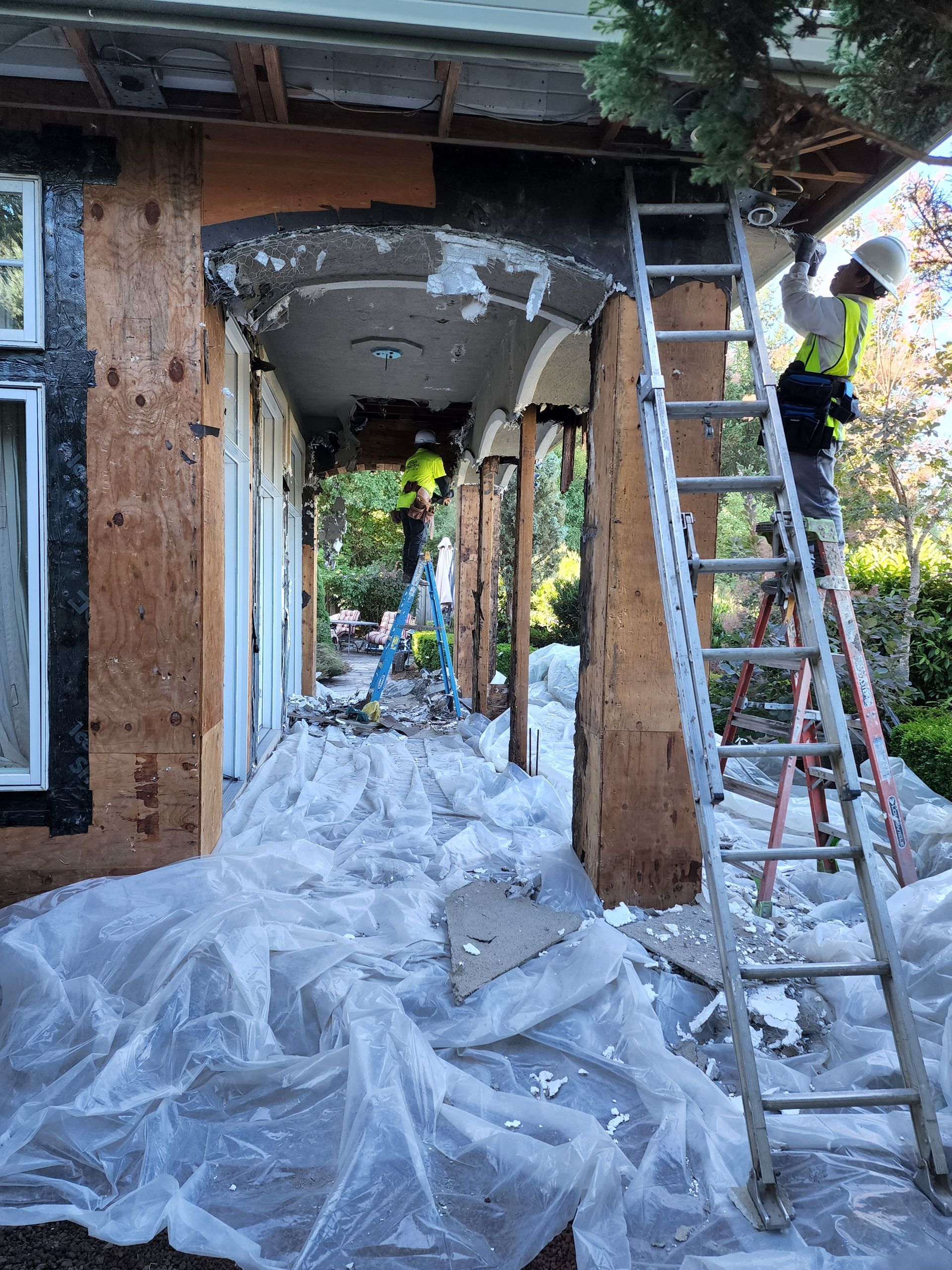 A man is standing on a ladder in front of a house under construction.