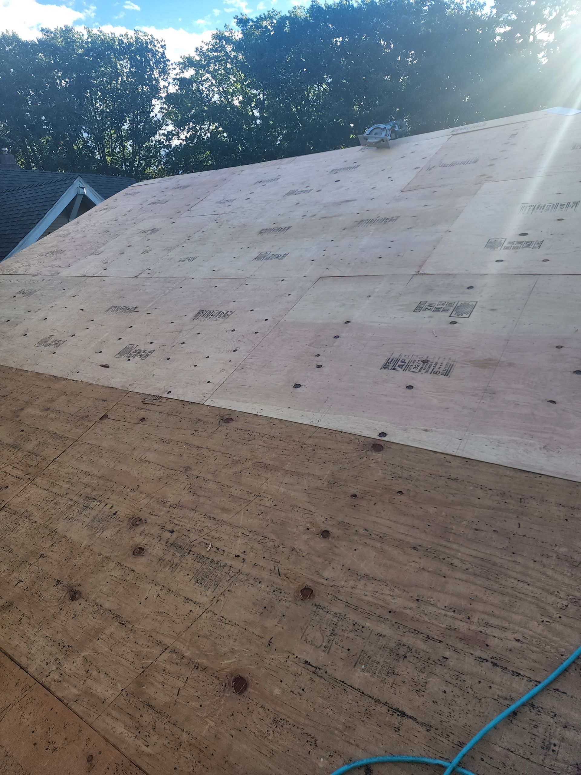The roof of a house is being built and the sun is shining through the trees.