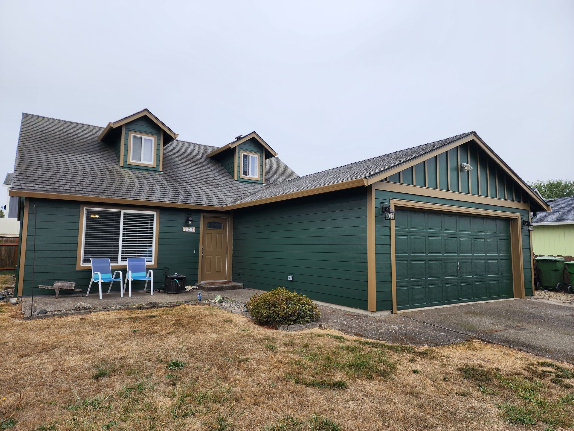 A green house with a garage and a table and chairs in front of it.