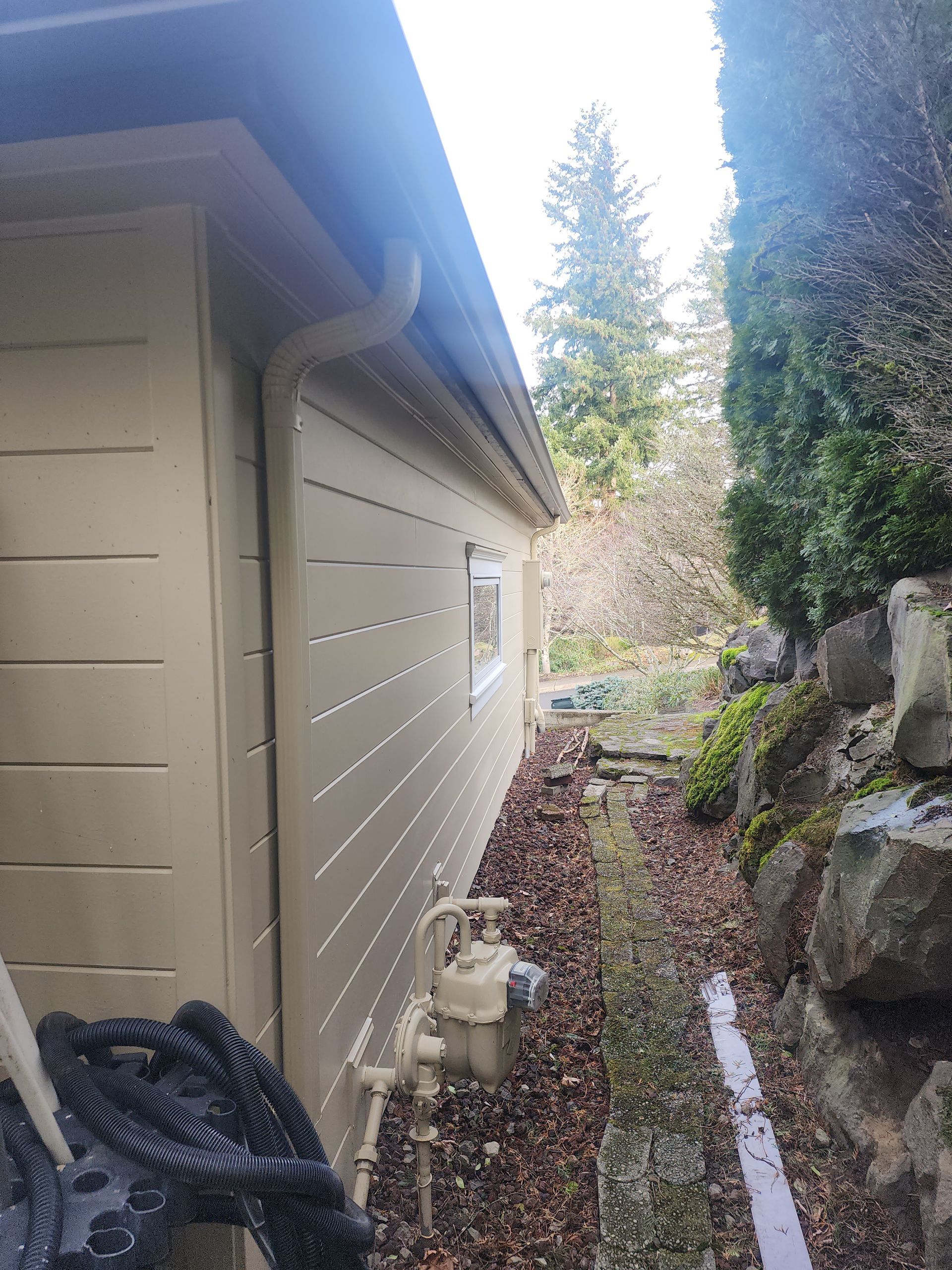 A house with a gutter on the side of it and a gas meter on the side of it.