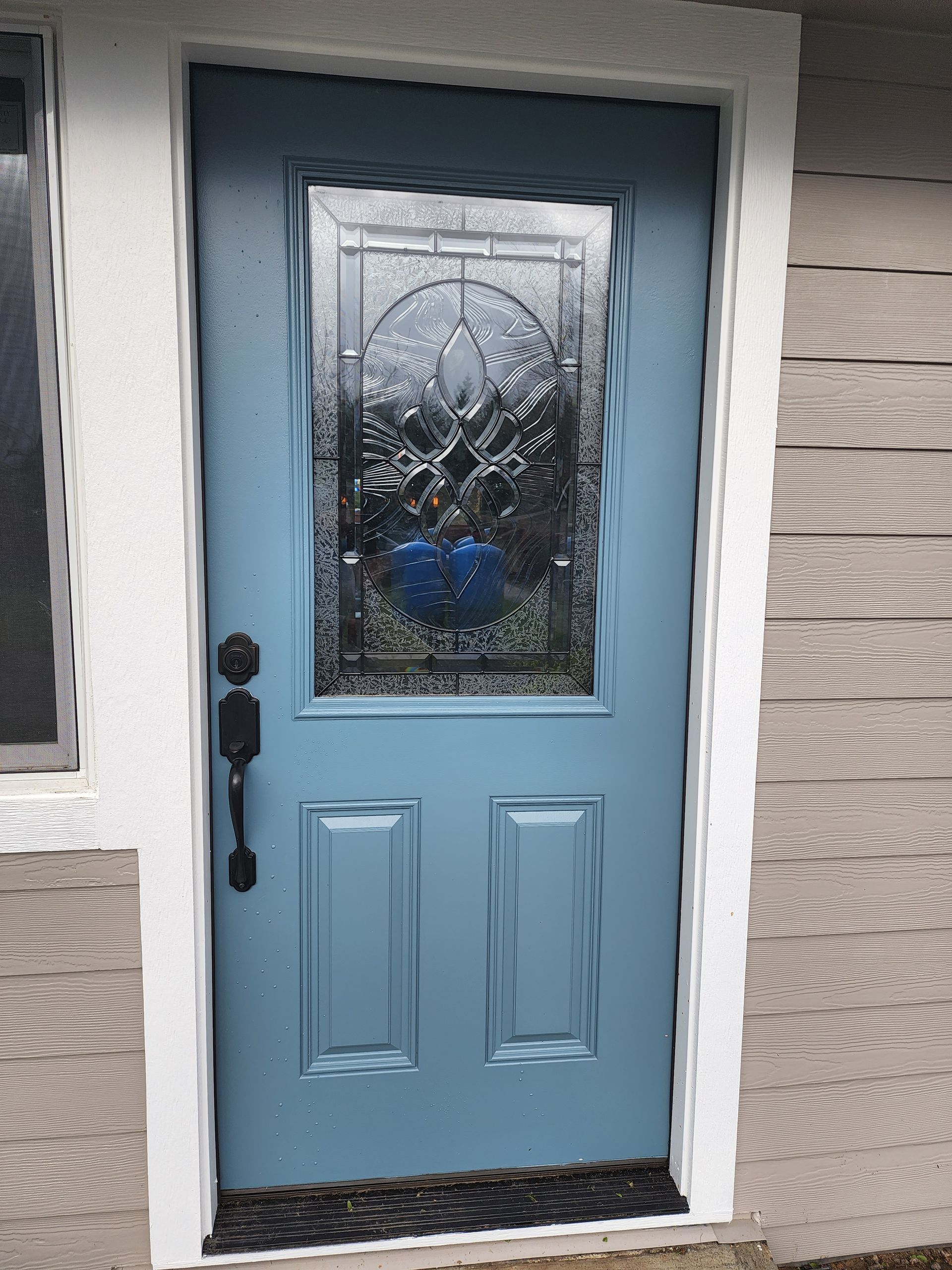A blue door with a stained glass window is on a house.
