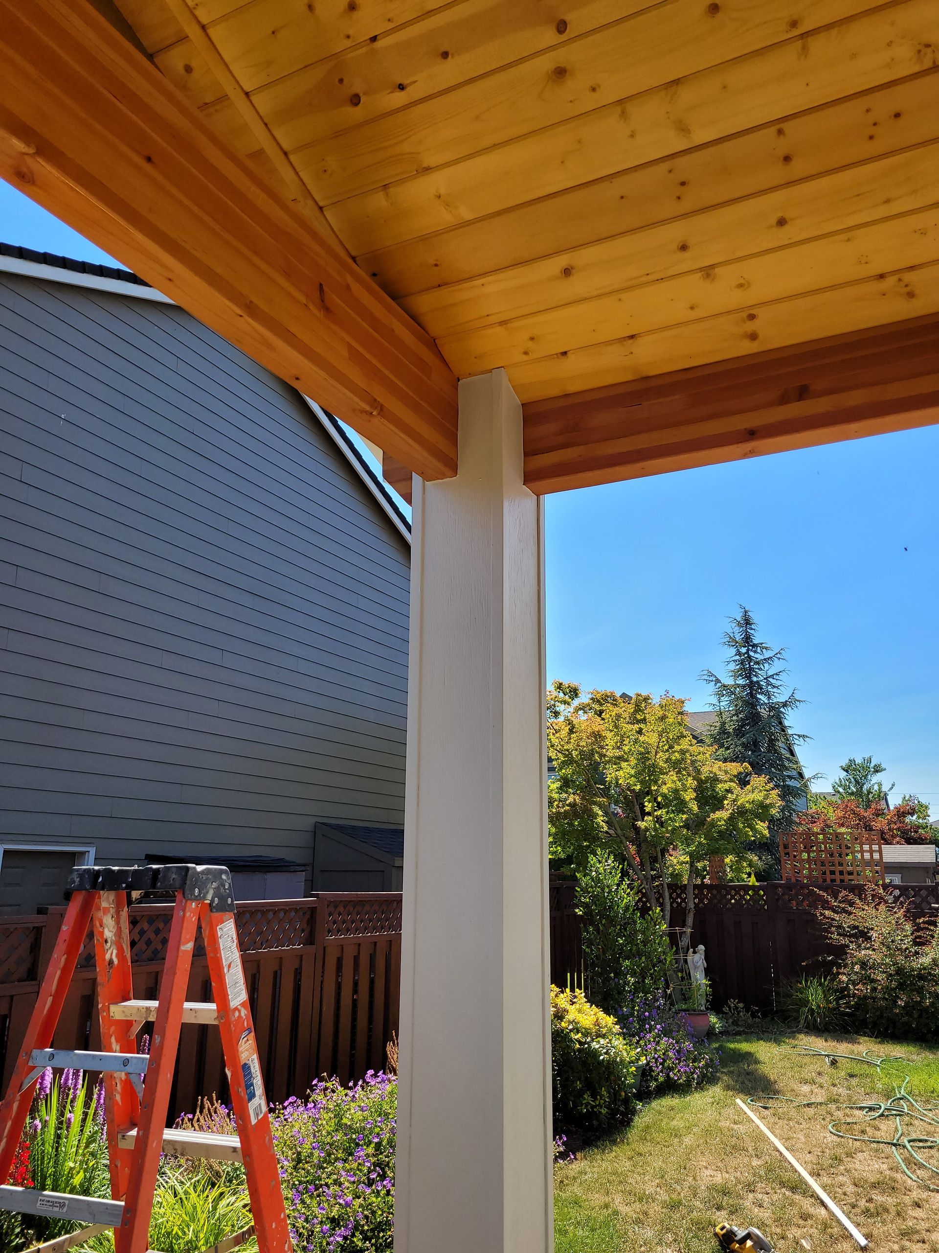A ladder is sitting under a wooden roof in a backyard.