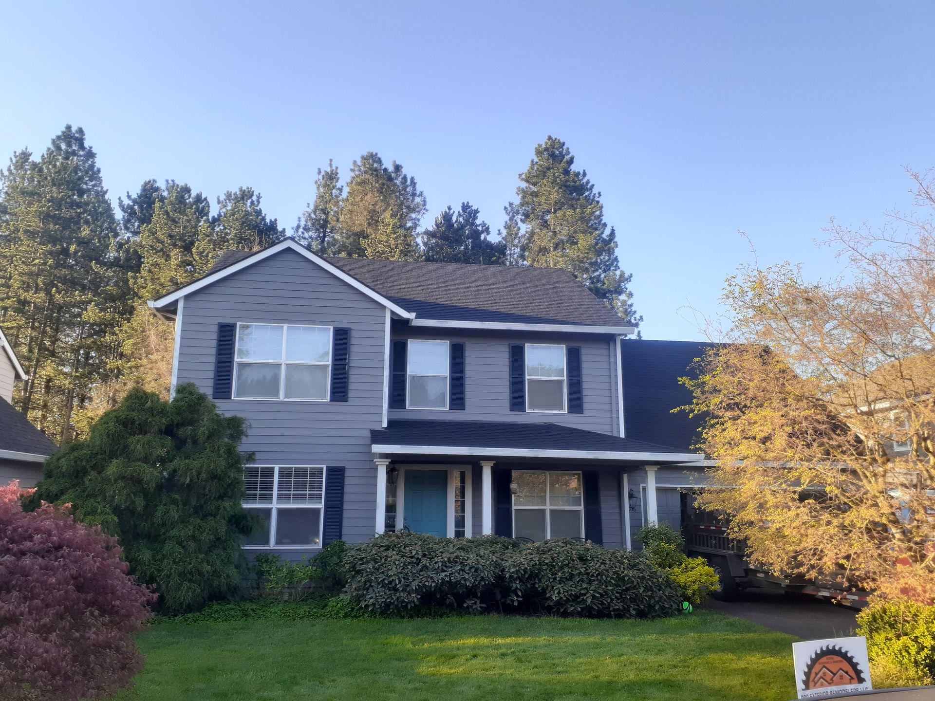 A gray house with black shutters and a sign in front of it