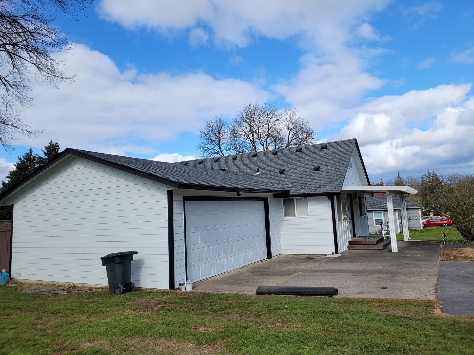 A white house with a black garage door and a gray roof.