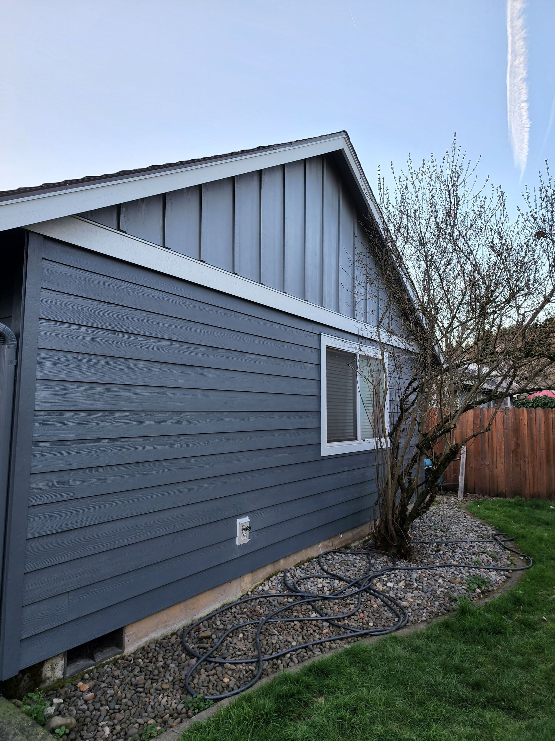 A house with a gray siding and a tree in front of it.