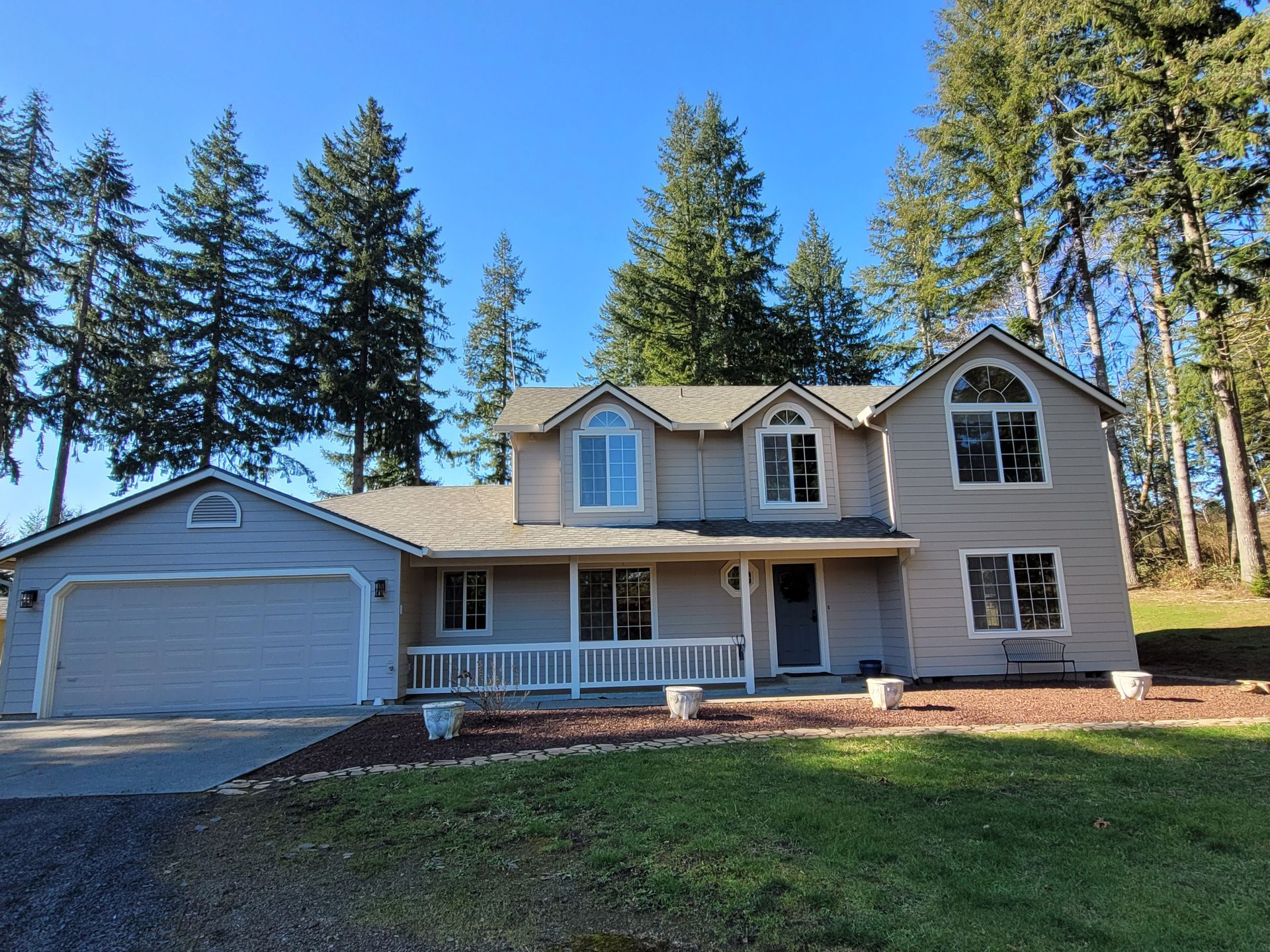 A large house with a garage and a porch surrounded by trees