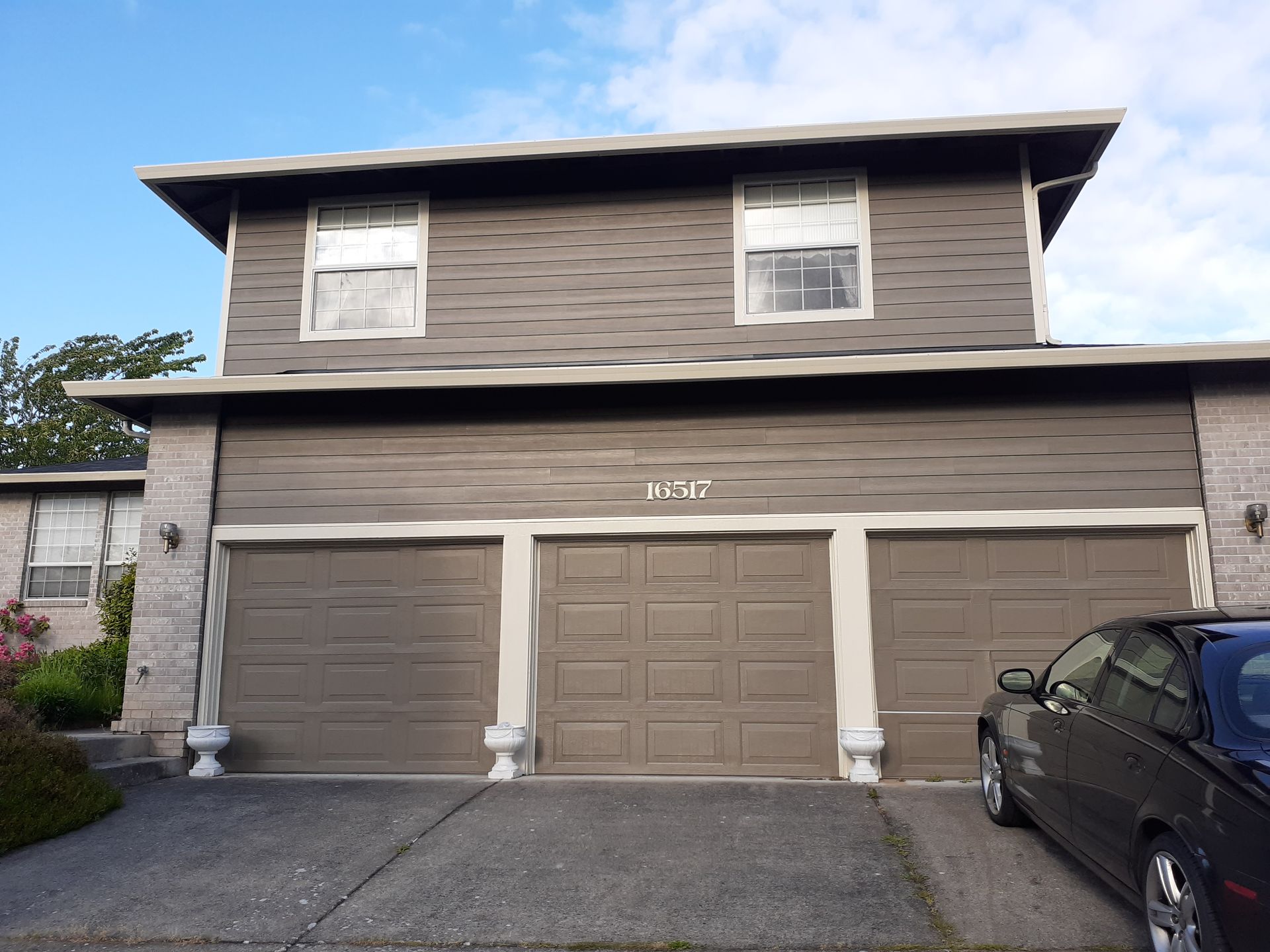 A car is parked in front of a house with three garage doors