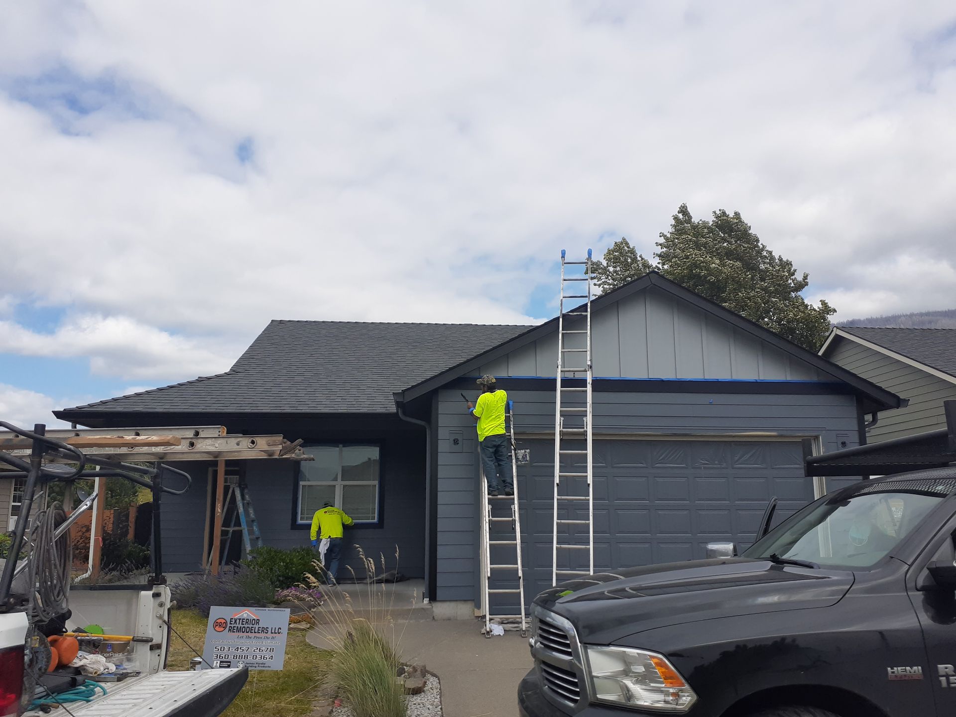 A man on a ladder is painting the side of a house.