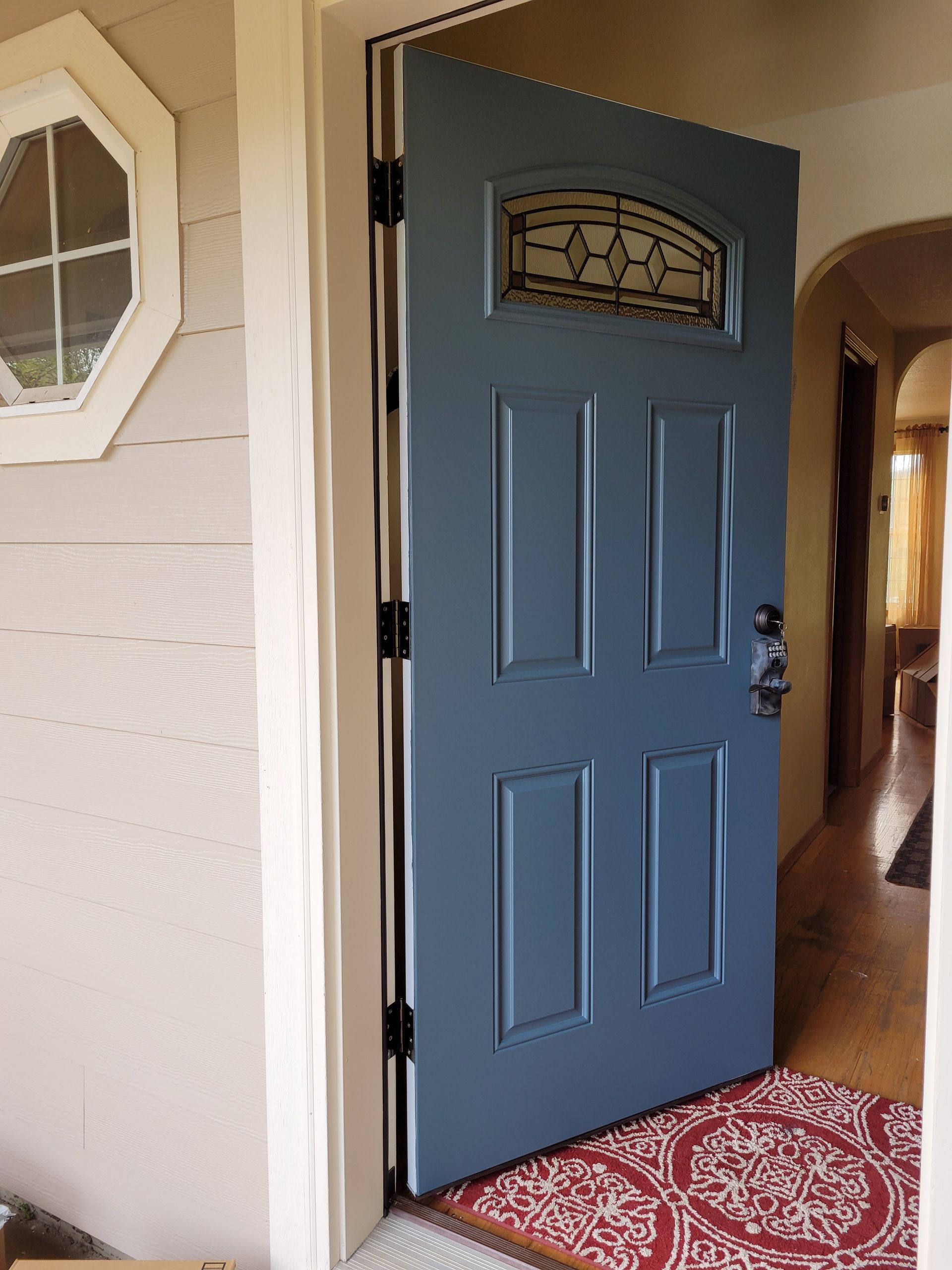 A blue door with a stained glass window is open in a house.
