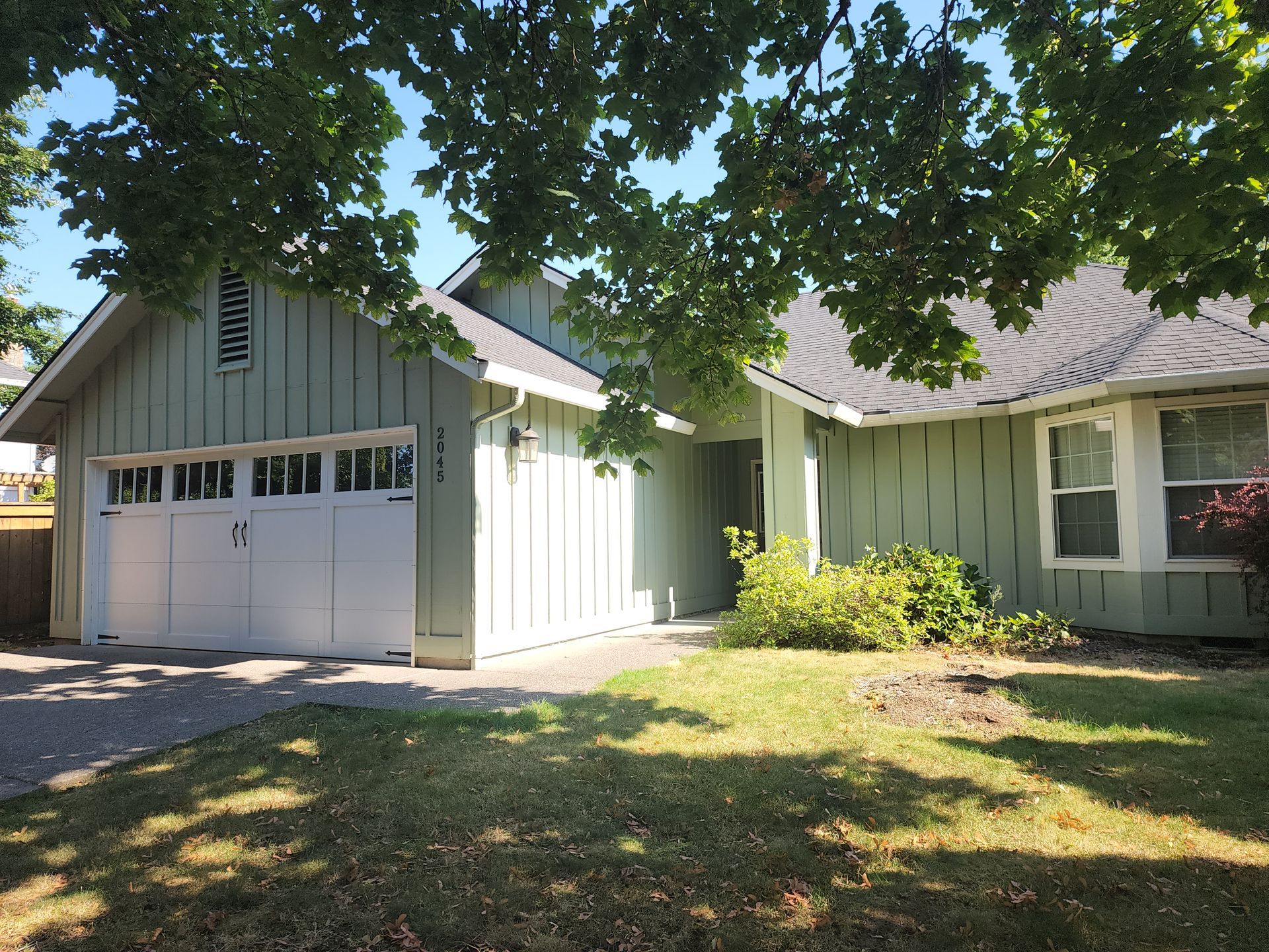 A green house with a white garage door and a tree in front of it.
