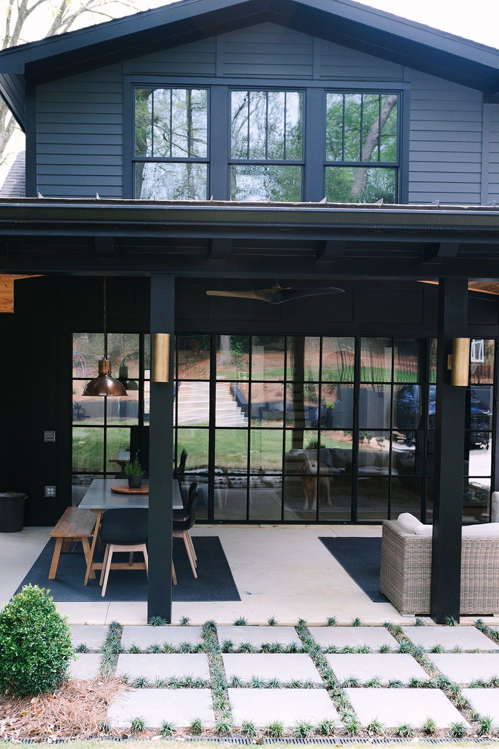 A black house with a large porch and lots of windows.