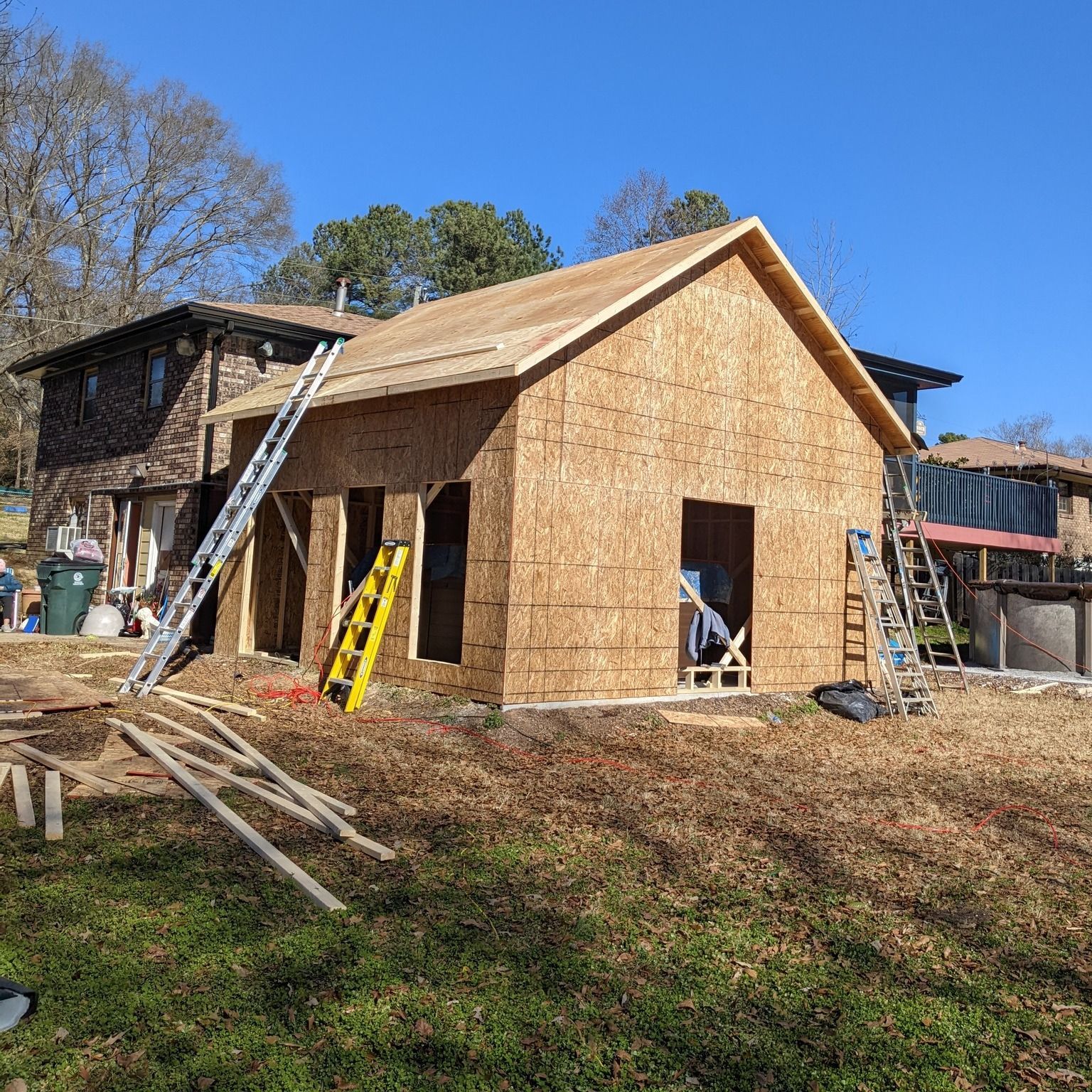 A house is being built with plywood and a ladder in the backyard.