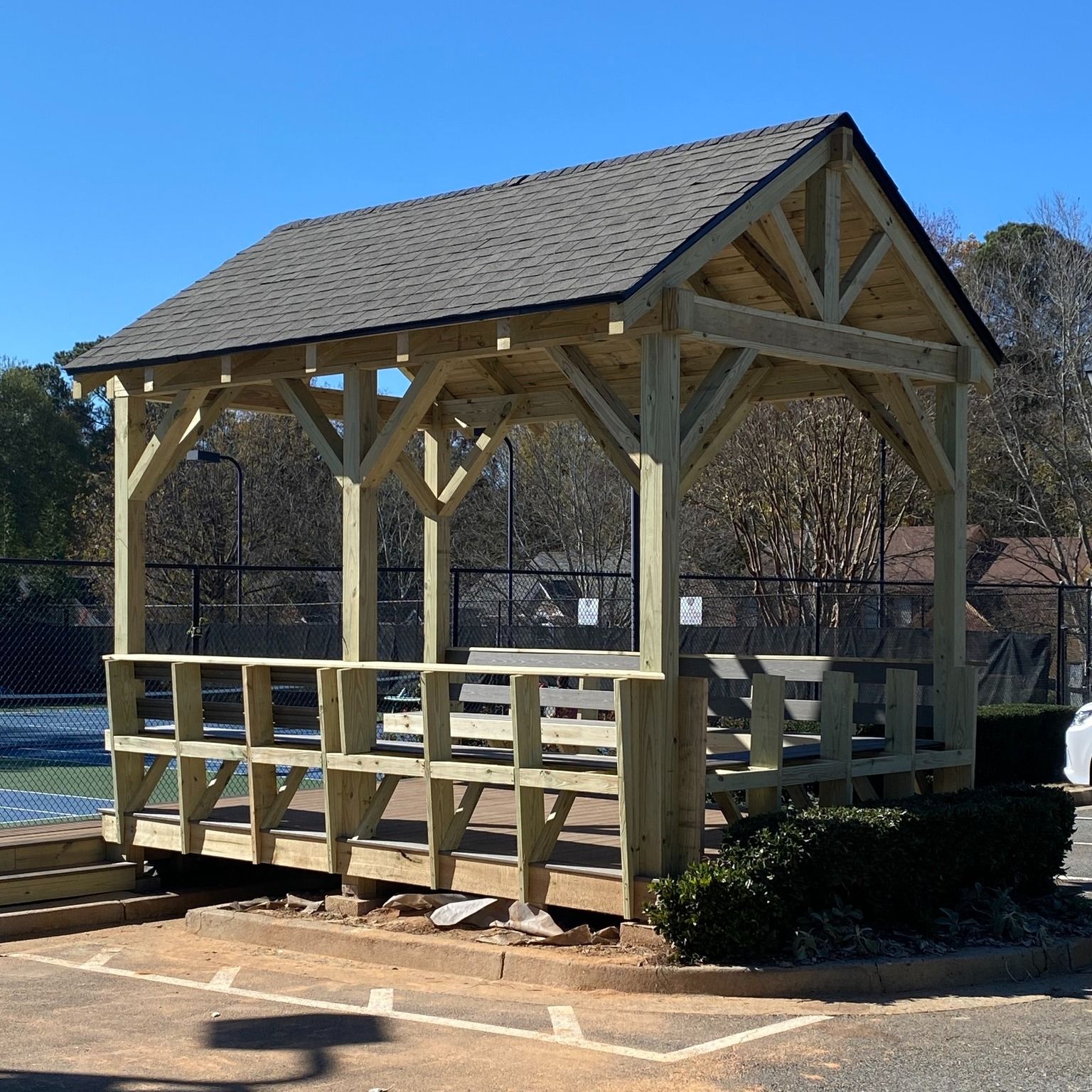 A wooden gazebo with a roof sits in a parking lot