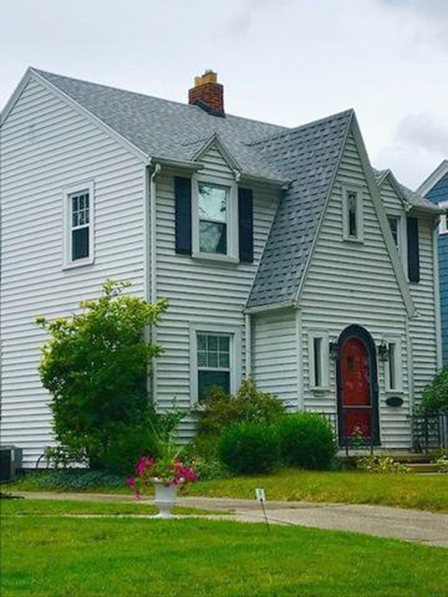 White house with dark gray roof, red door, black shutters, green lawn and shrubs