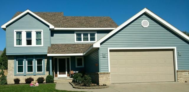 Blue-sided house with tan garage door, brown roof, and white trim against a bright blue sky.