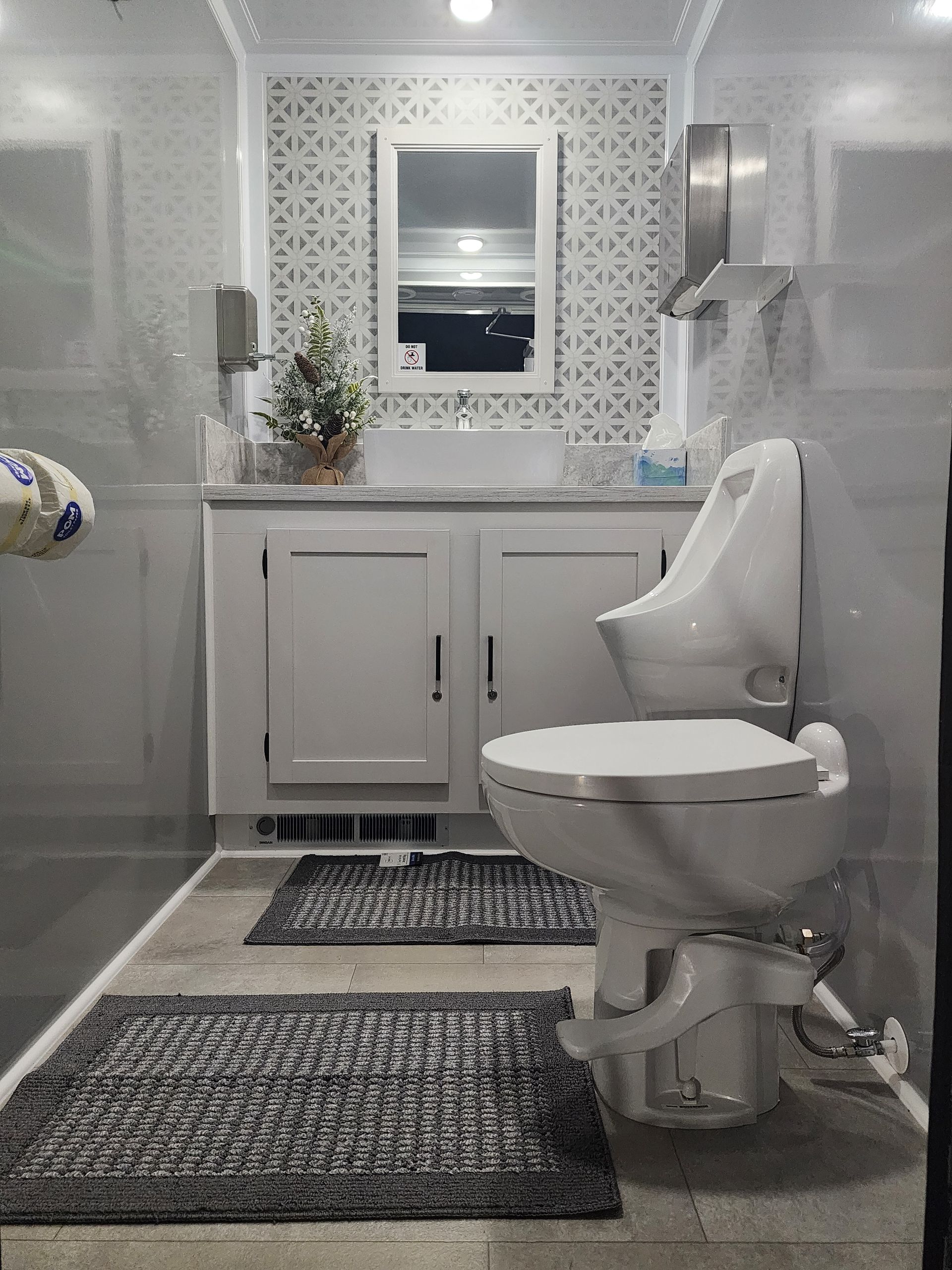 Modern white bathroom with shower, vanity, toilet, patterned rug, and window