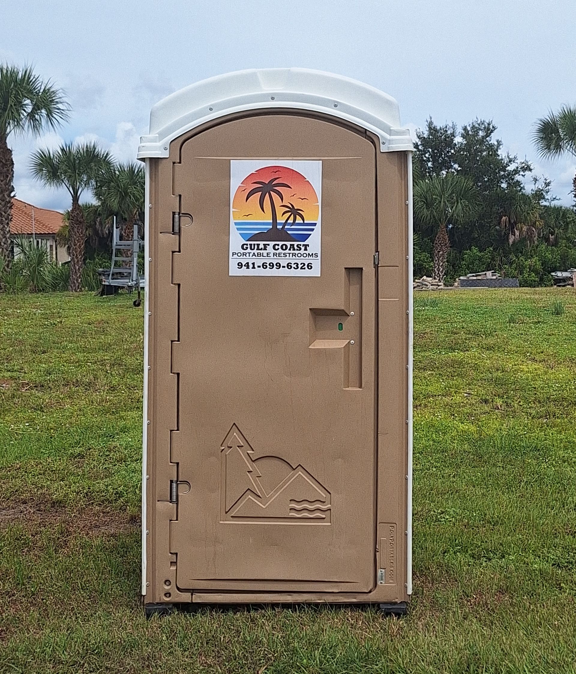 Beige portable toilet in a grassy outdoor area with trees in the background.