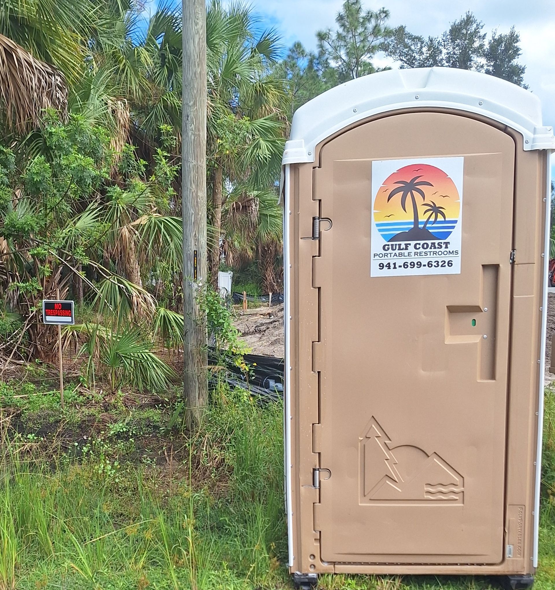 Beige portable toilet beside dense greenery, with a sunset logo sign on the door.