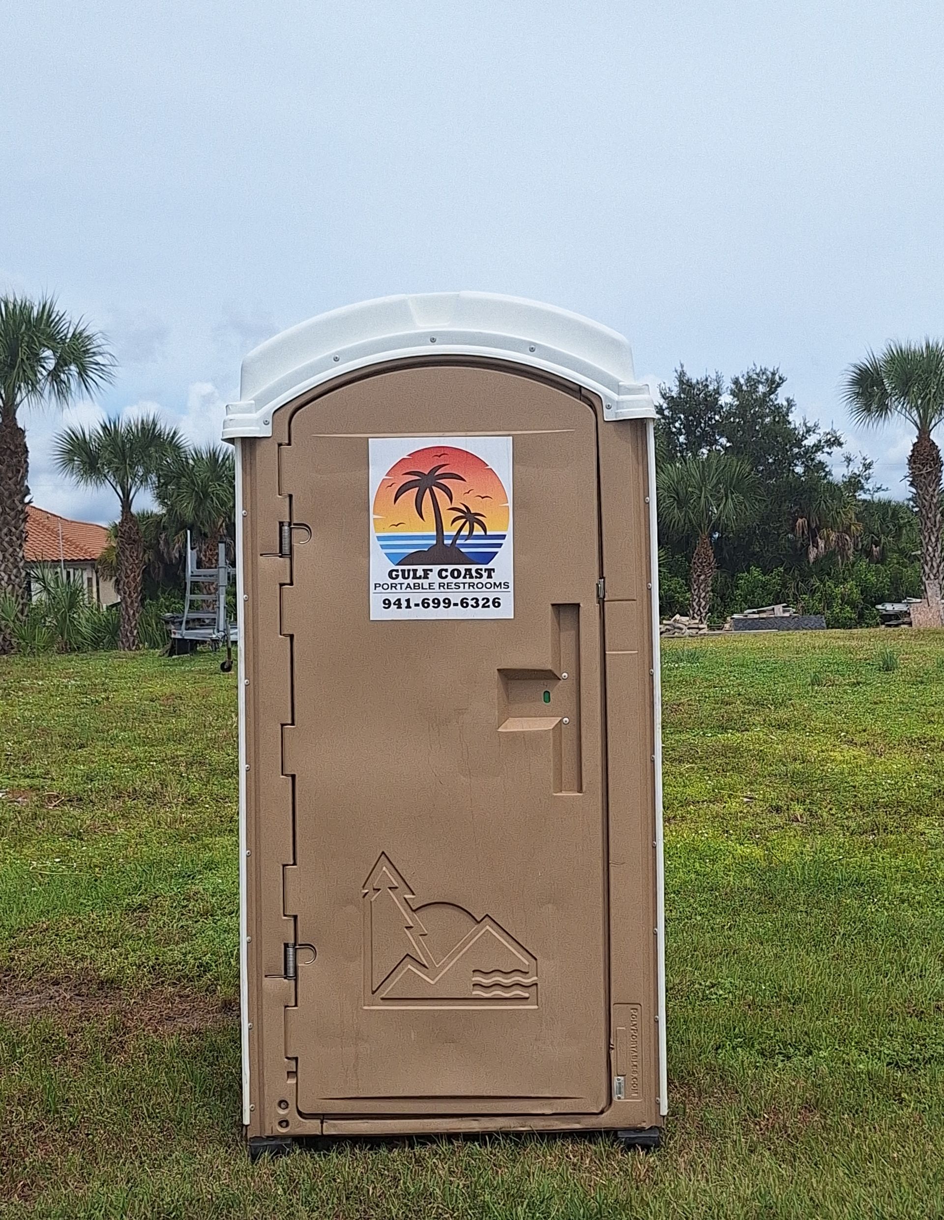 Portable toilet with a sign on the door, standing outdoors on grass under a cloudy sky