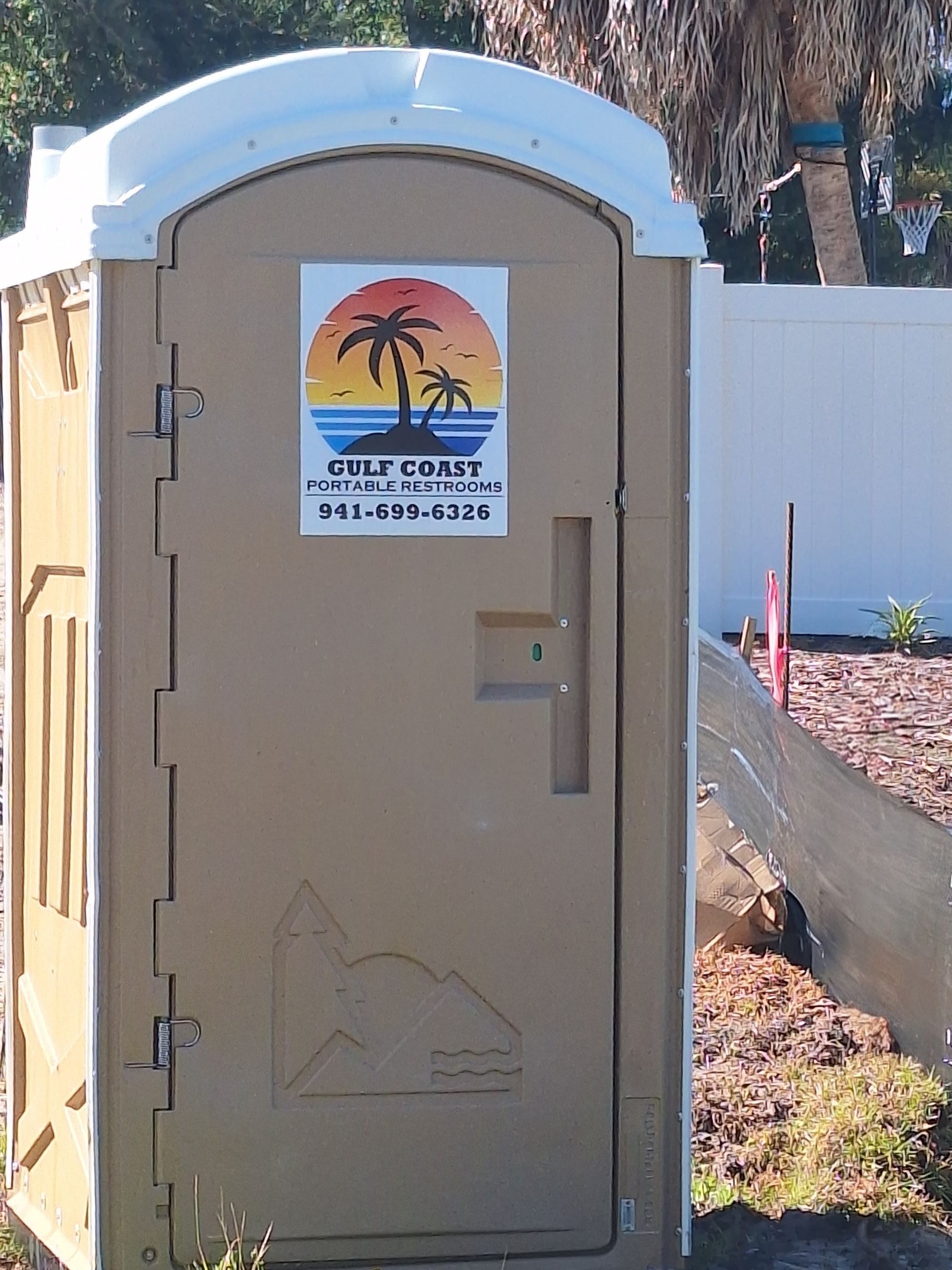 Portable restroom with a “Swift Spill” sign, beige door, and blue roof outdoors near a fence.