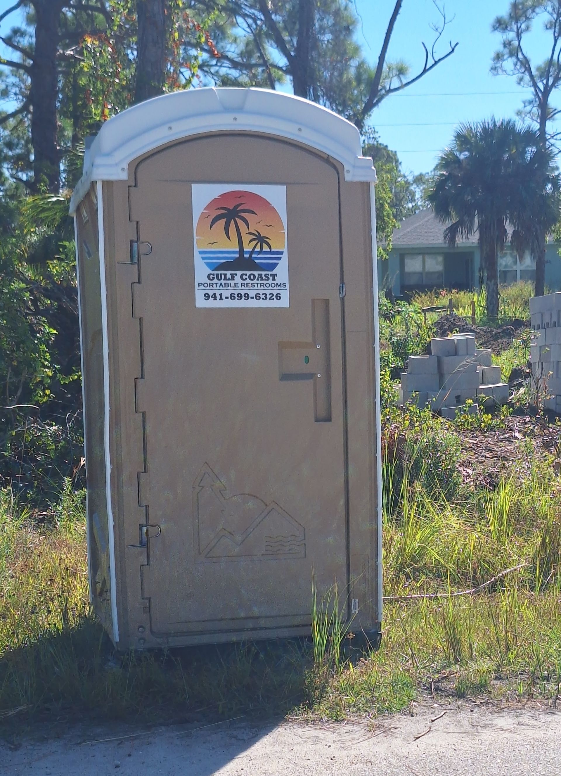 Portable toilet beside a cemetery path, with trees and gravestones in the background.