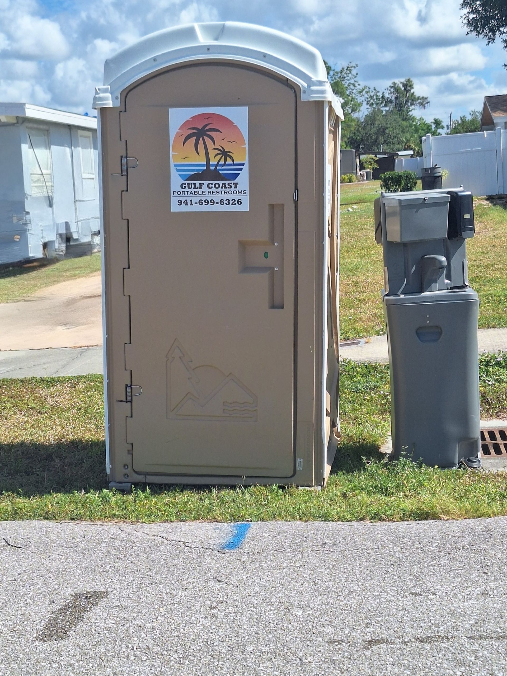Portable toilet beside a gray utility box on a grassy roadside under a cloudy sky