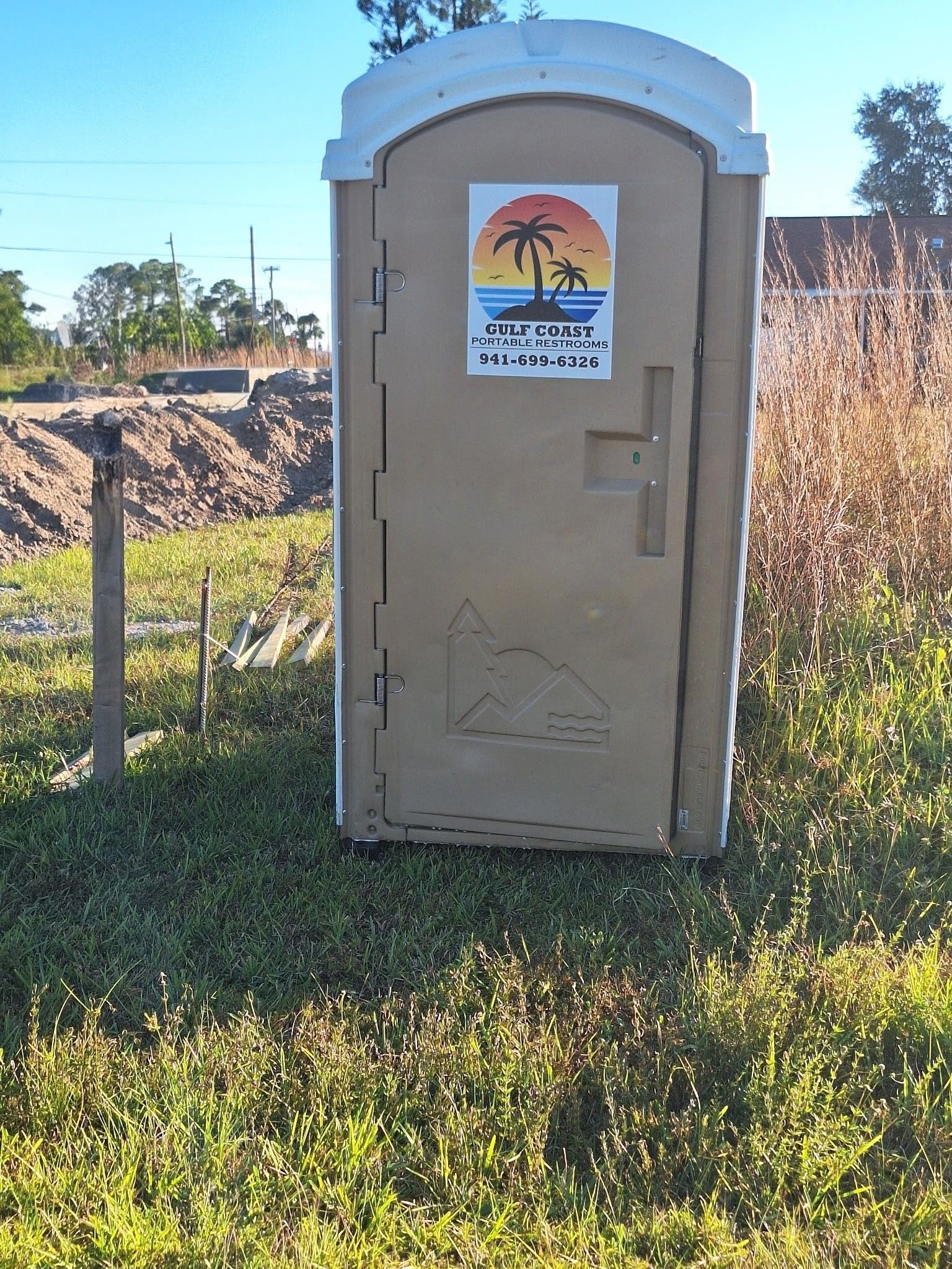 Portable toilet in a grassy field with a sunset sticker on the door